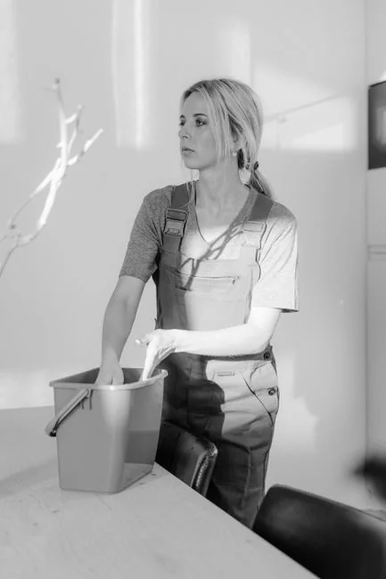 a-woman-in-a-green-shirt-and-black-gloves-vacuuming-a-gray-ottoman-5txz228u4eo